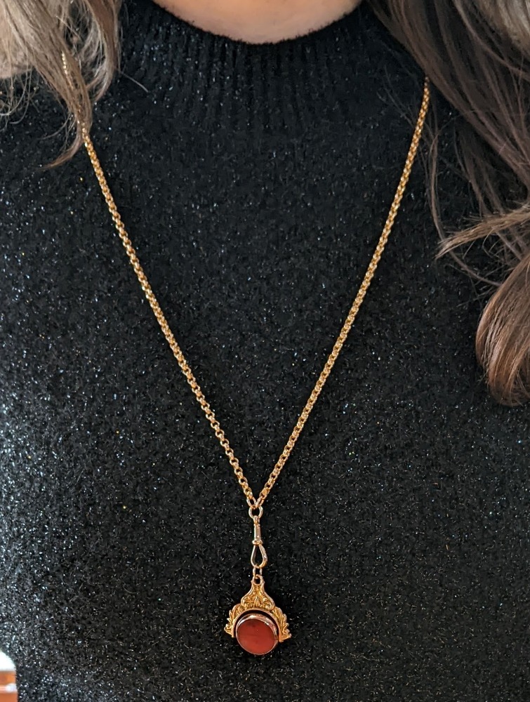 Gold chain necklace with an ornate gold pendant and a round red gemstone against a sparkly black top.