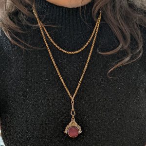 Gold layered necklaces with a pendant featuring a pink circular gemstone on a black glittery sweater.