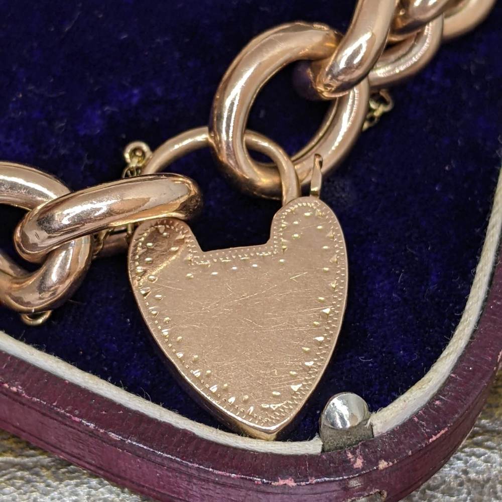 Close-up of a rose-gold heart pendant on a chunky chain inside a velvet jewelry box.