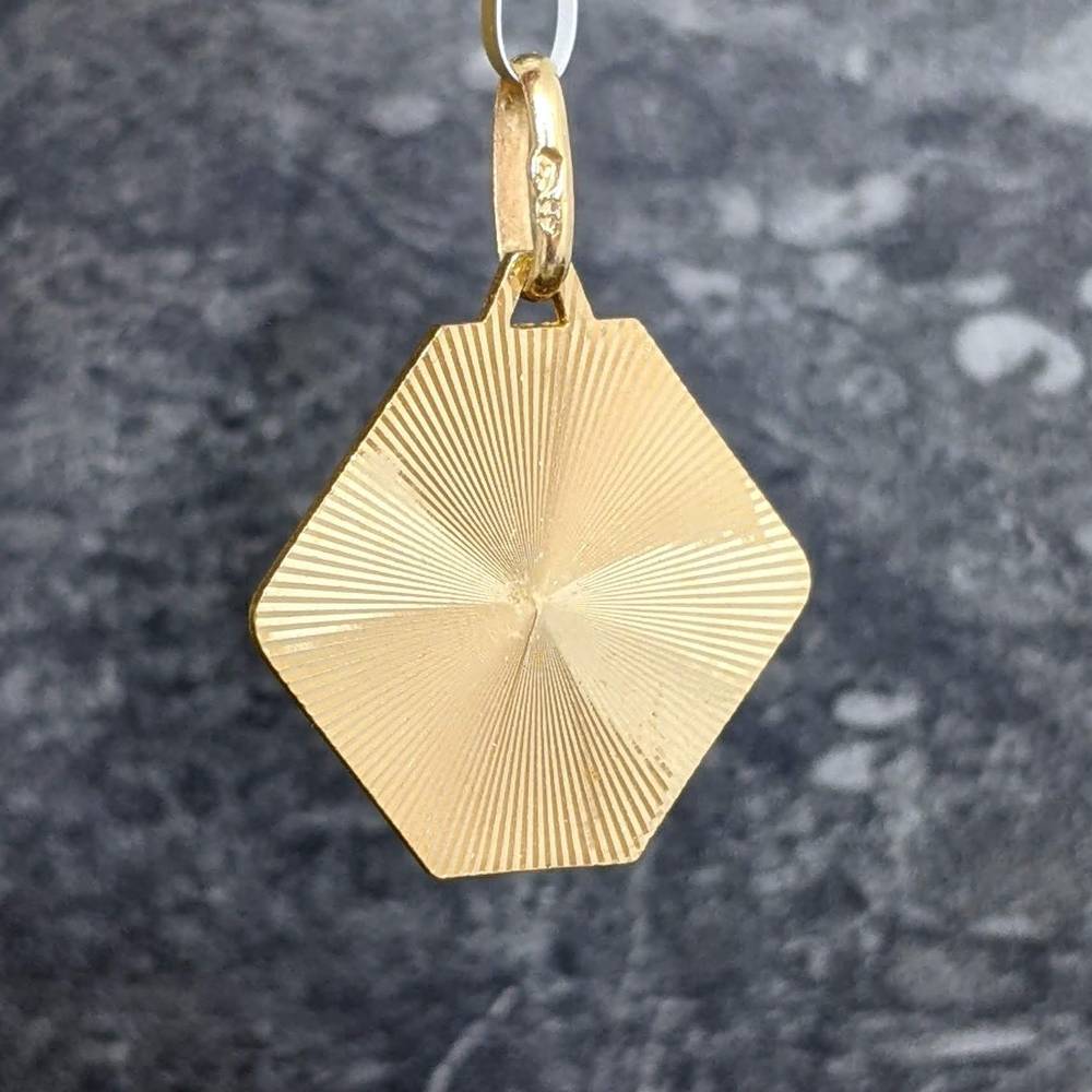 Gold diamond-shaped pendant with concentric radial lines hanging from a small loop in a blurry background.