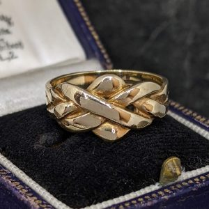 Gold braided ring resting on a black velvet ring box, showing an intertwined knot design.