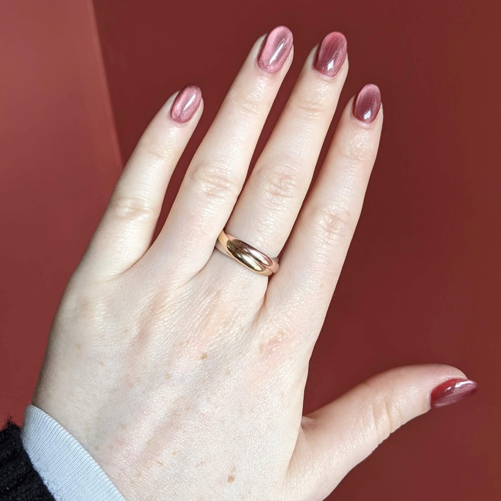 Close-up of a hand with two-tone pink and burgundy nails and a gold ring on the ring finger against a red background.