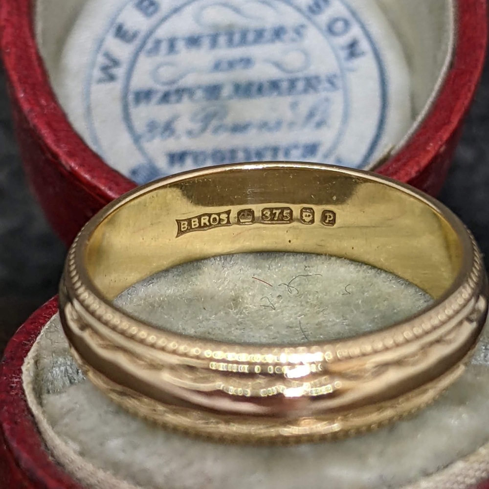 Gold wedding band with maker's mark 'B.BROS' and '375' gold fineness inside, in a red jewelry box.