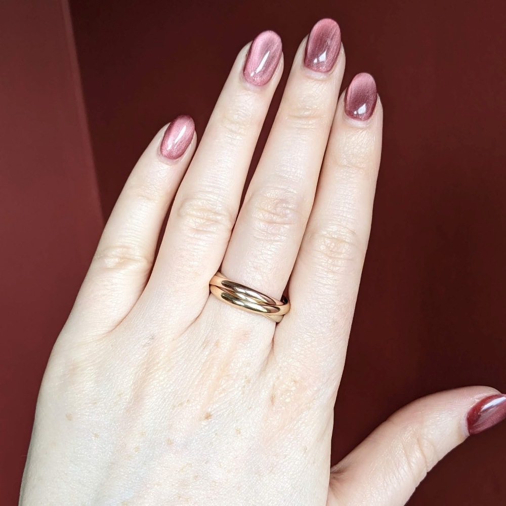 Close-up of a left hand with pink-mauve nail polish wearing a two-tone gold twisted band ring on the ring finger.