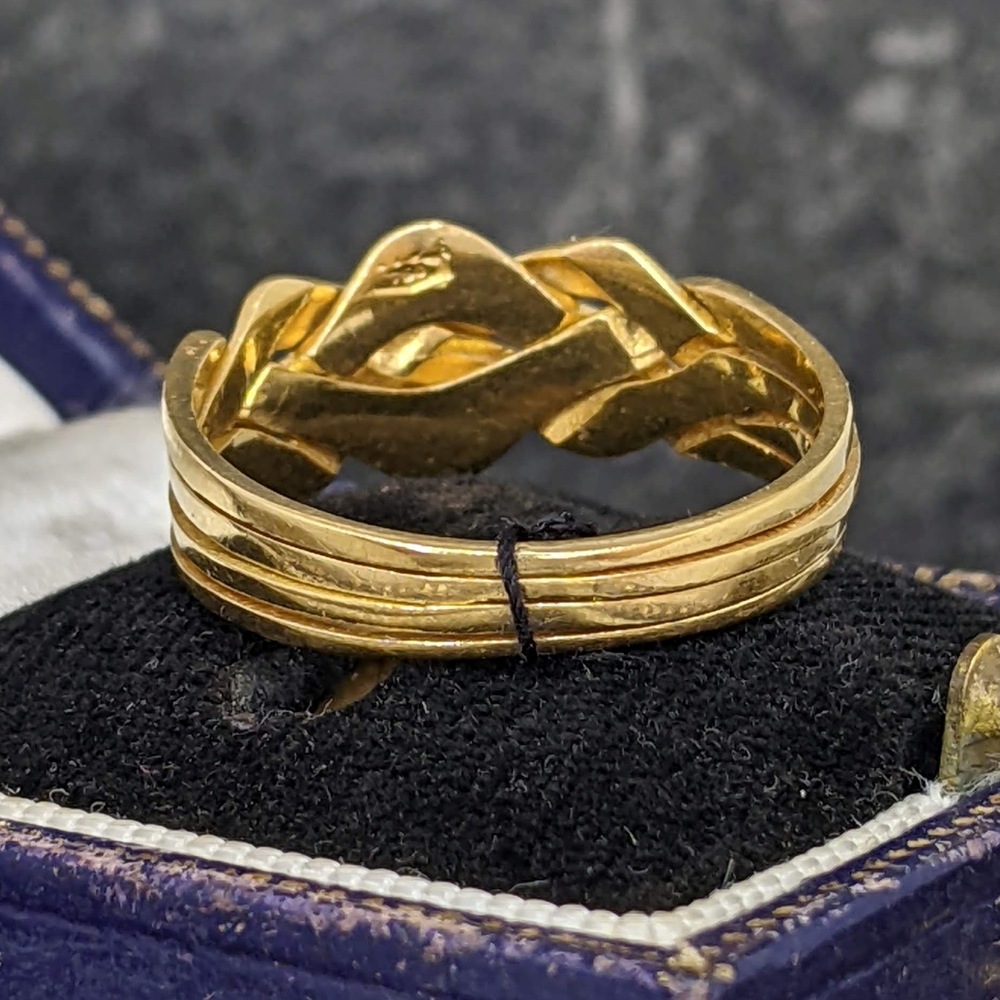 Close-up of a gold multi-band ring with a twisted, interwoven design, displayed in a blue jewelry box with black lining.