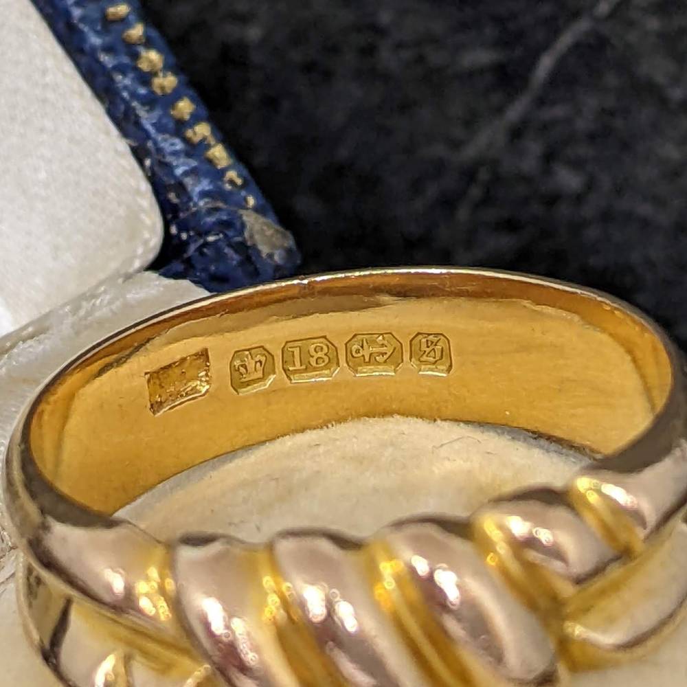 Close-up of a ring's inner band showing hallmarks, including 18K gold stamp and additional maker marks.