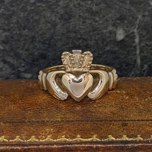 Two-tone ring with a heart centerpiece and a crown on top, resting on wood surface.