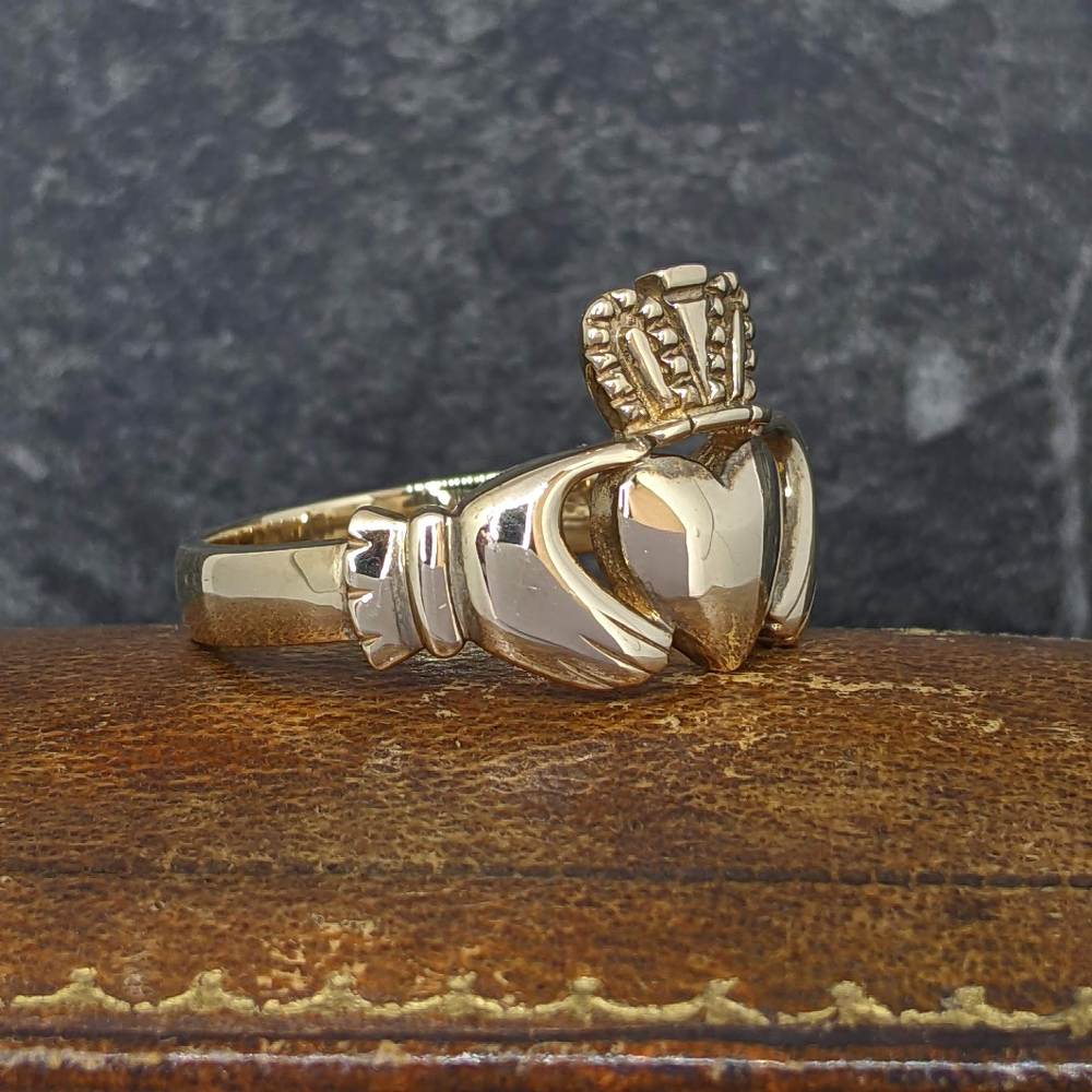 Gold signet ring with a heart-shaped gemstone and crown-like detailing, resting on wood surface.