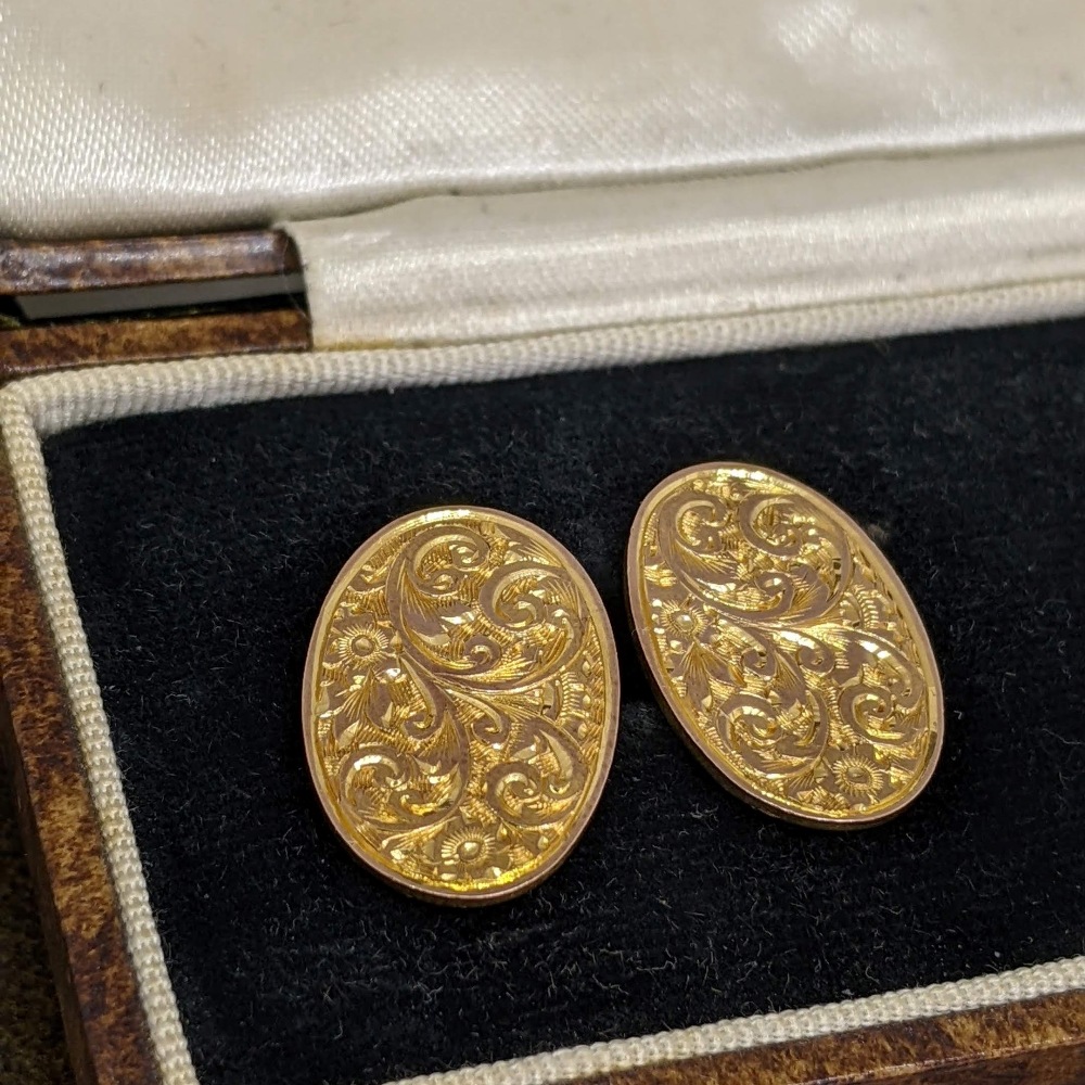 Pair of gold oval cufflinks with intricate floral scroll engraving in a velvet-lined jewelry box