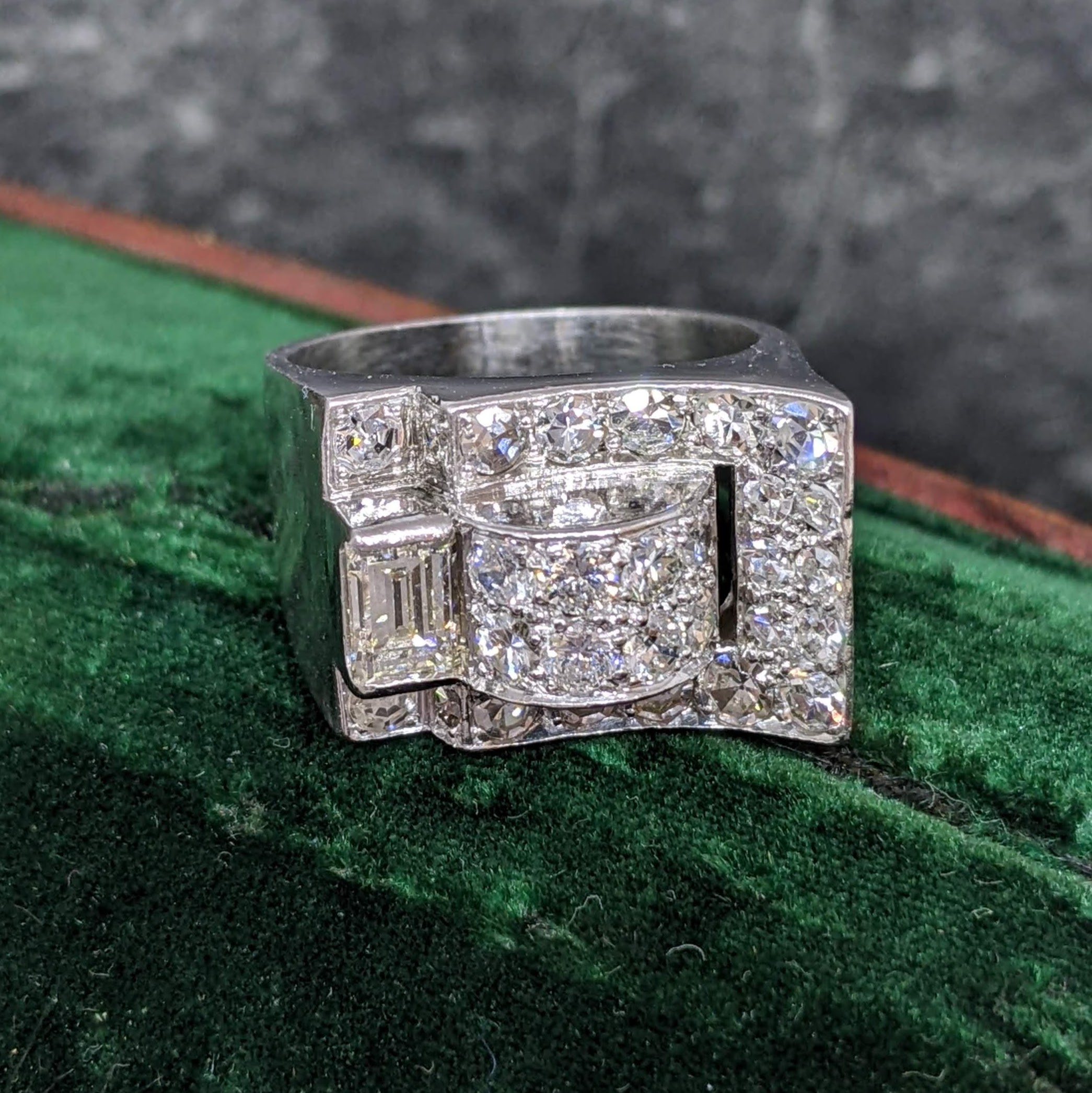 Close-up of a silver, diamond-cut ring resting on a green textured surface, showing sparkling facets.