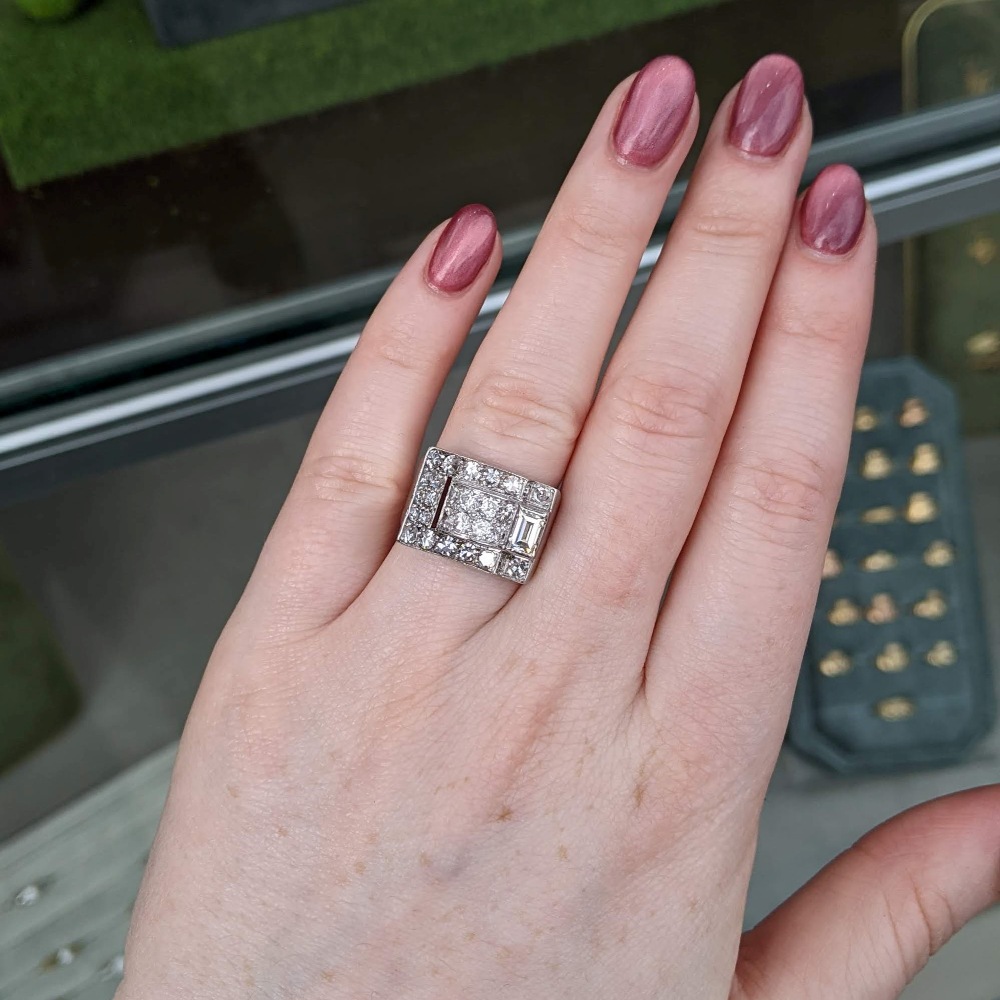 Close-up of a hand with a square halo diamond ring on the ring finger, nails painted pink.