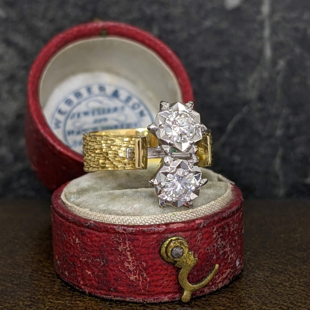 Two-diamond vintage-style ring with a gold band in a red velvet ring box, diamonds set centerpiece side by side in silver prongs.