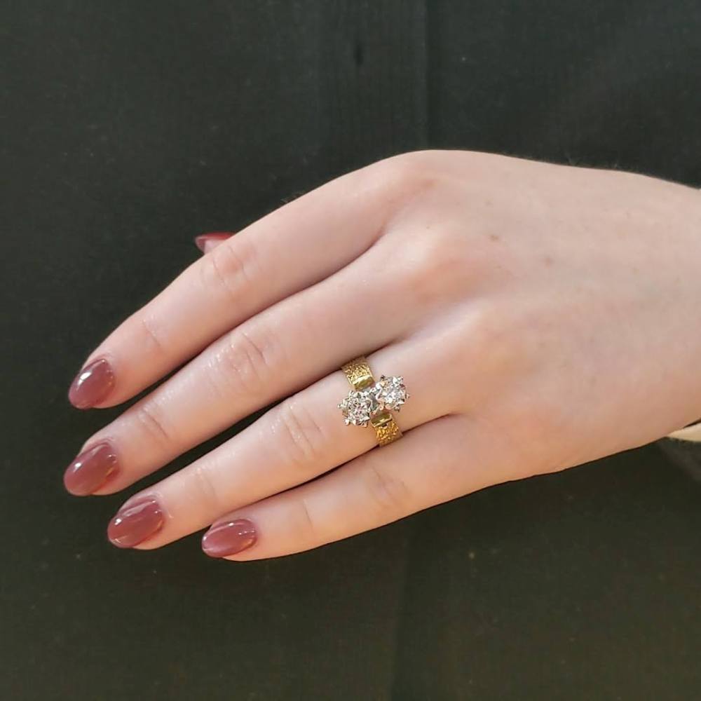 Hand with a gold ring featuring two clusters of diamonds on the ring finger.