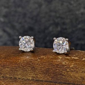 Two diamond stud earrings with four-prong settings resting on a wooden surface.