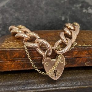 Rose gold bracelet with chunky links and a heart-shaped padlock charm on a wooden surface.