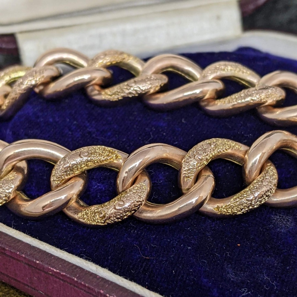 Close-up of a thick gold chain with textured, engraved links resting on royal blue velvet in a jewelry box display.