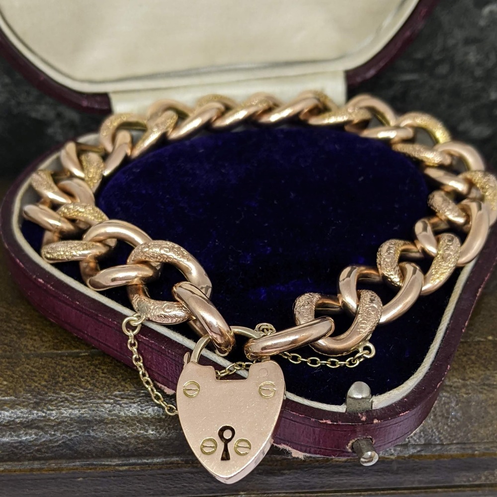 Rose-gold heart-shaped padlock pendant on a chunky chain, resting in an open purple jewelry box lined with dark blue velvet.